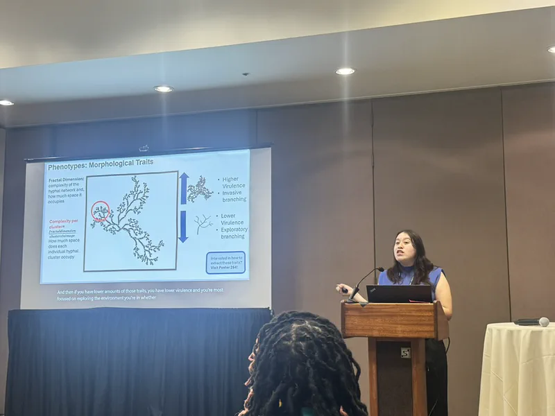 A lab member presenting a fungal network diagram and morphological traits at a conference lectern.