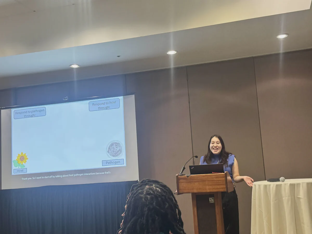 A researcher smiling at a lectern beside her research slides.