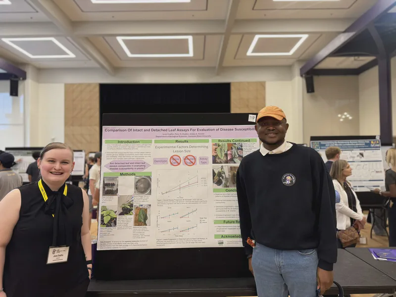 A student and mentor beside a poster about plant–pathogen interactions.