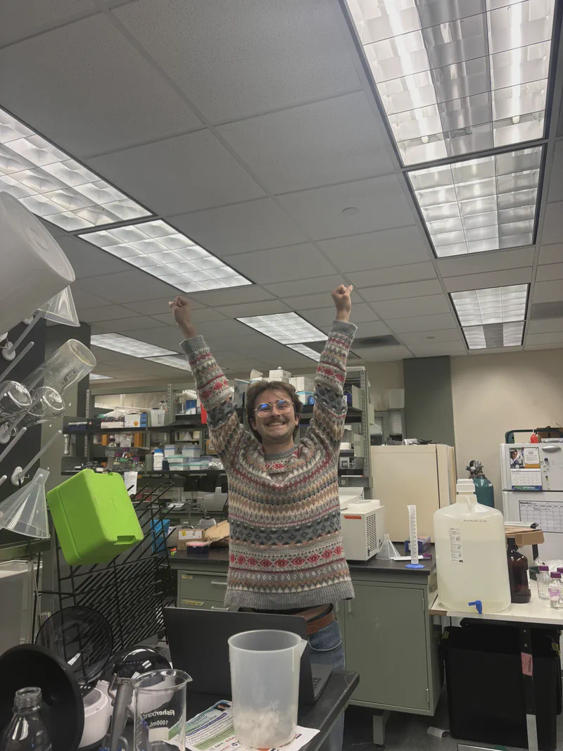 Justin celebrating in the laboratory with both arms raised.