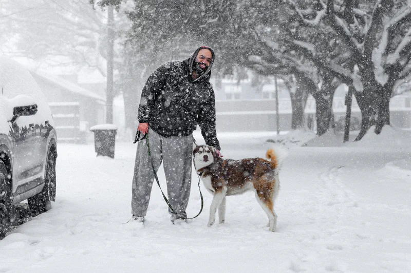 Jordan Dowell smiling beside a dog during heavy snowfall.