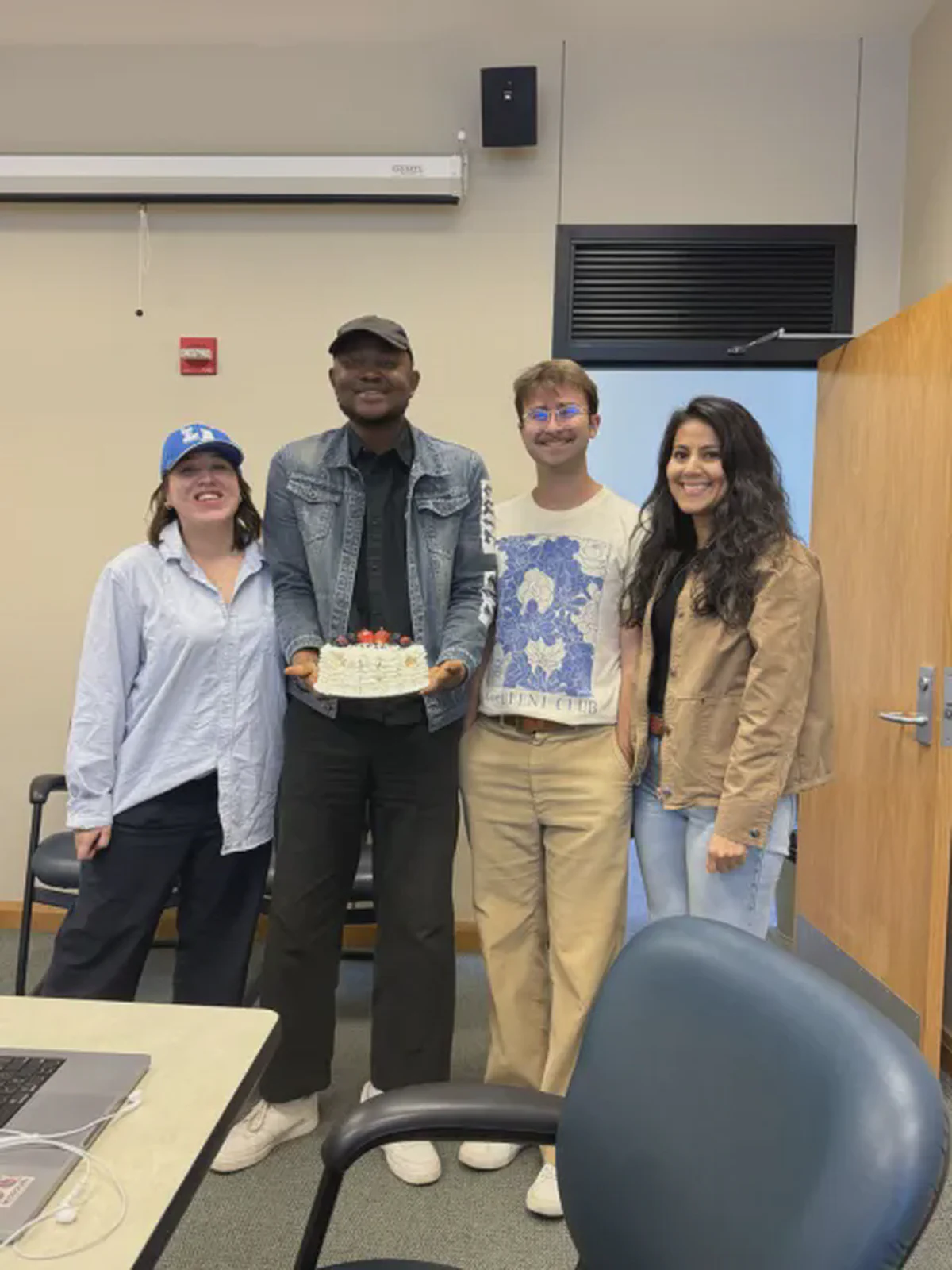 Four lab members smiling together, with one holding a birthday cake.