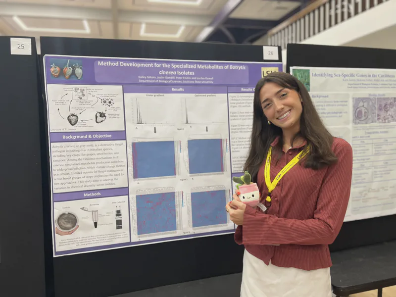 A student smiling beside her scientific poster.