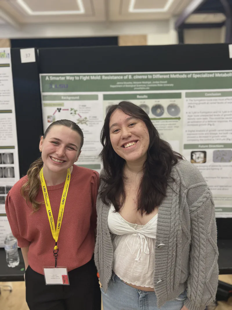 Two lab members smiling beside a research poster.