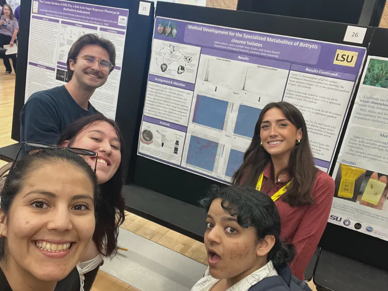 A group selfie in front of a student research poster.
