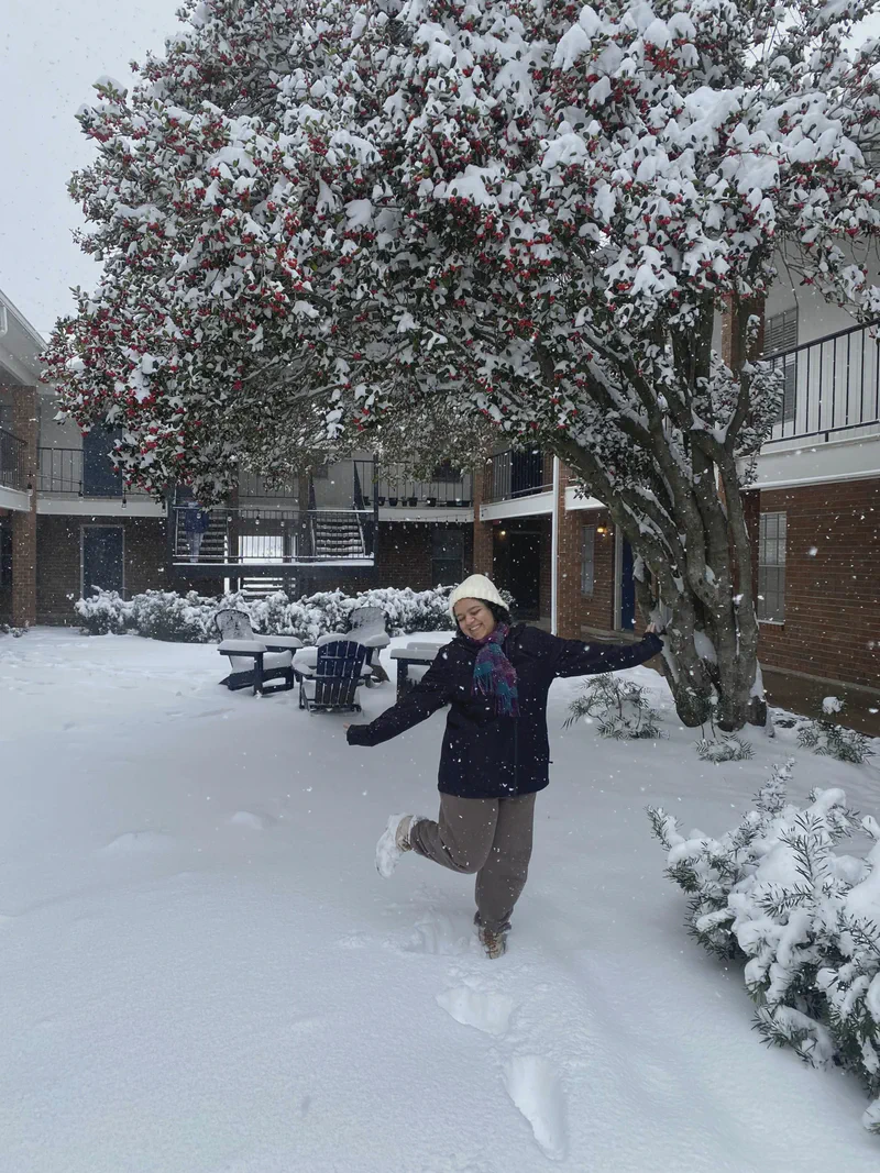 A lab member standing with arms outstretched among snow-covered trees.