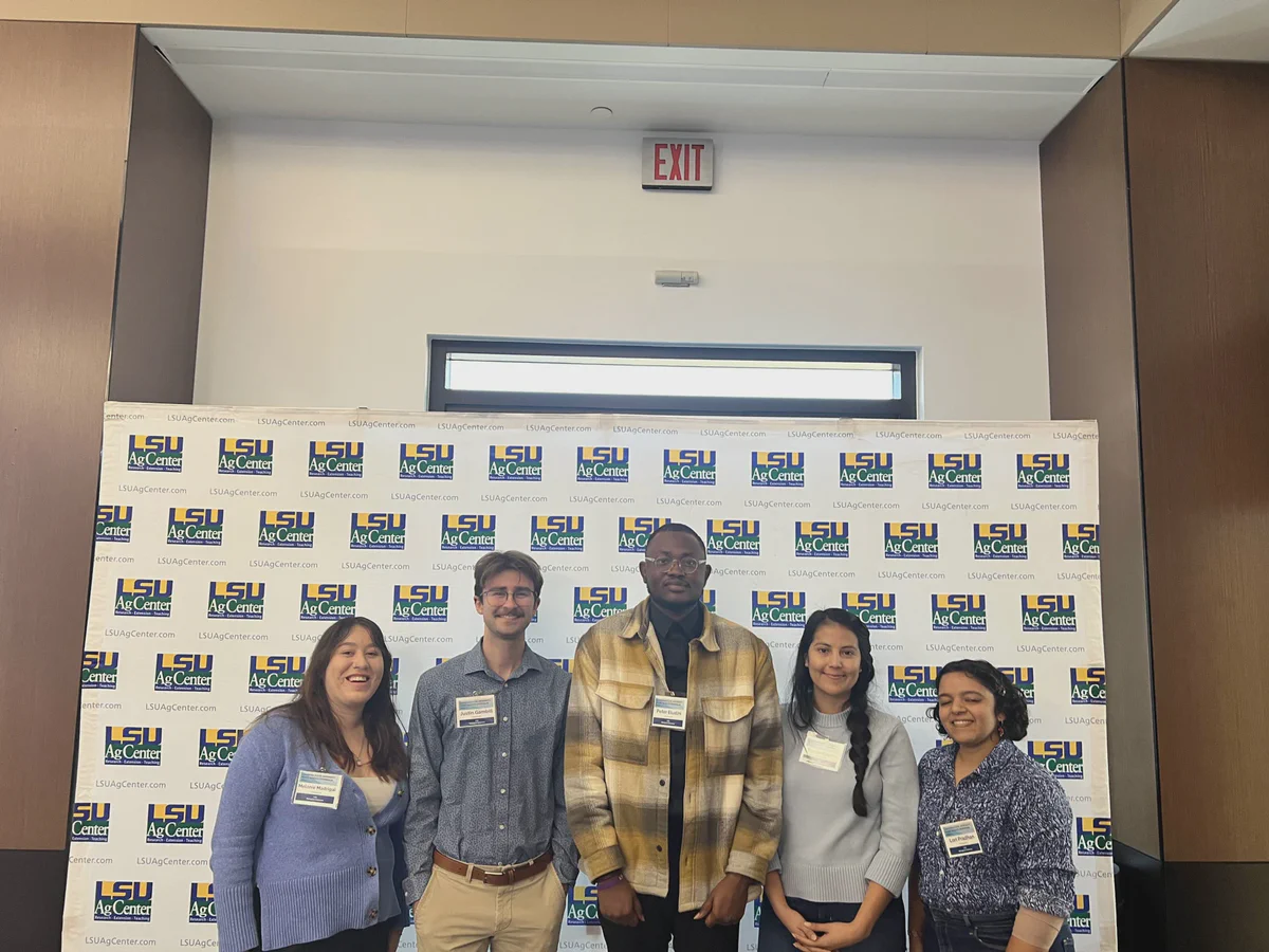 Five lab members posing in front of an LSU backdrop.
