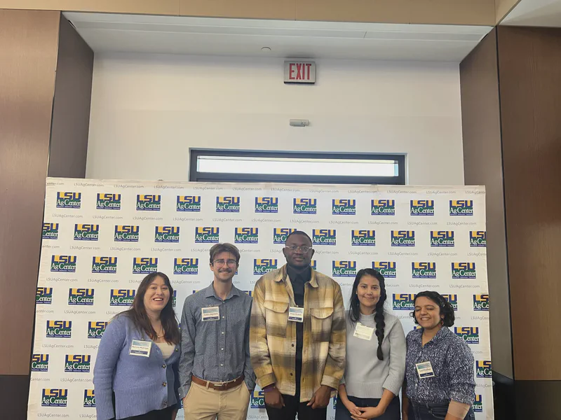 Five lab members posing in front of an LSU backdrop.