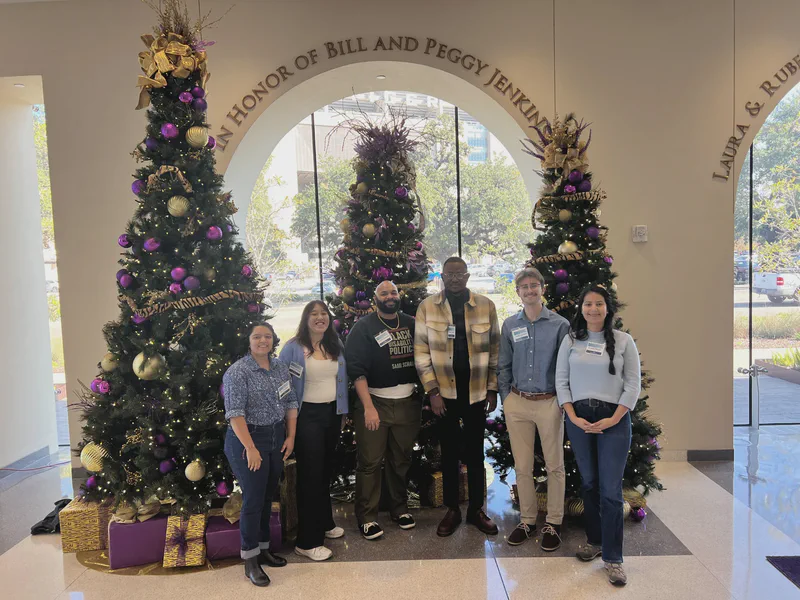 Lab members standing together beside purple and gold holiday trees.